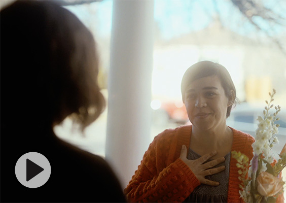 A kindly woman, flowers in hand, visits a grieving neighbor.