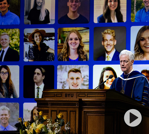 President Kevin Worthen speaks at the Marriott Center podium in front of a video display of graduates he  qualified as super because they were resilient, durable, and adaptable throughout a global pandemic.