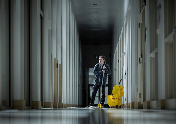 An image of a custodian with a mop and bucket in a hallway,illustrating less visible essential workers. Photo by Nate Edwards/BYU Photo.