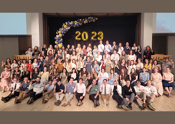 The 2023 graduating class of first-generation college students pose for a photo. Each of them holds up one finger to signify their place as the first generation of their family to graduate from college. Photo by Joe Wirthlin.