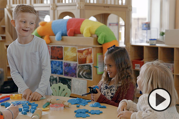 Three young children play with blue play dough at a table in the BYU Child and Family Studies Lab.