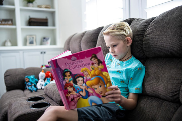 A young boy sits on a couch and reads from a collection of princess stories. Photo by Nate Edwards/BYU Photo.