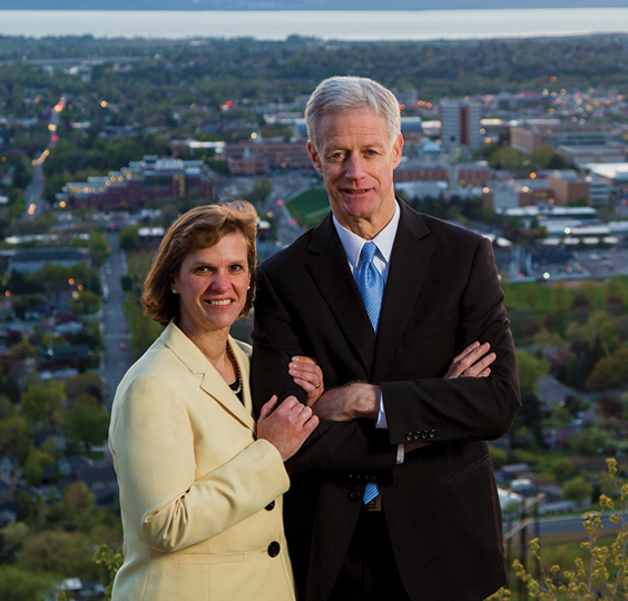 Kevin J and Peggy Worthen in suits stand on a Provo mountain, south BYU campus in the background.