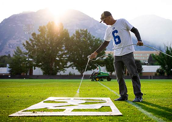 A BYU employee paints a large number onto the turf of the practice field.
