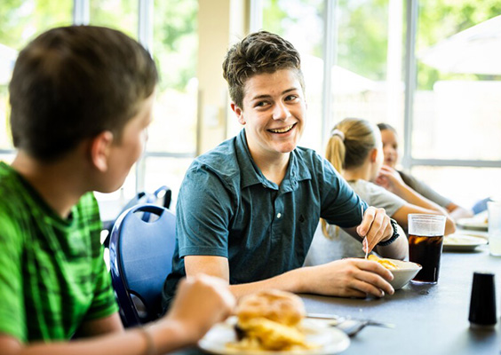 A young student smiles at a friend at lunchtime.