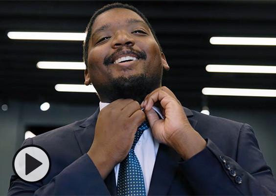 A young man in a new suit smiles while adjusting his collar and tie.