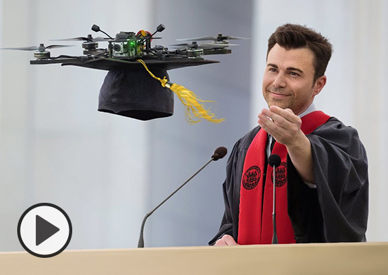 Mark Rober in black robes and a red sash reaches out to capture his graduation cap attached to a drone during his 2023 MIT commencement speech.