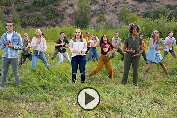 BYU's Young Ambassadors dance and sing in a grassy field.