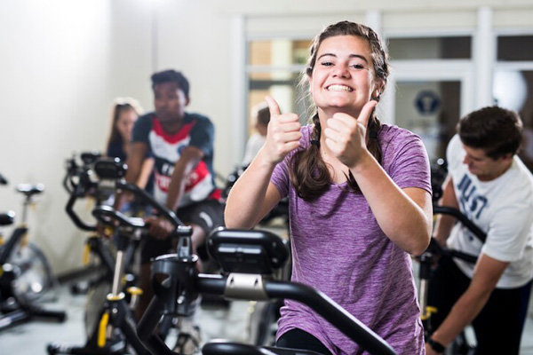 A smiling woman exercises on an spin bike.