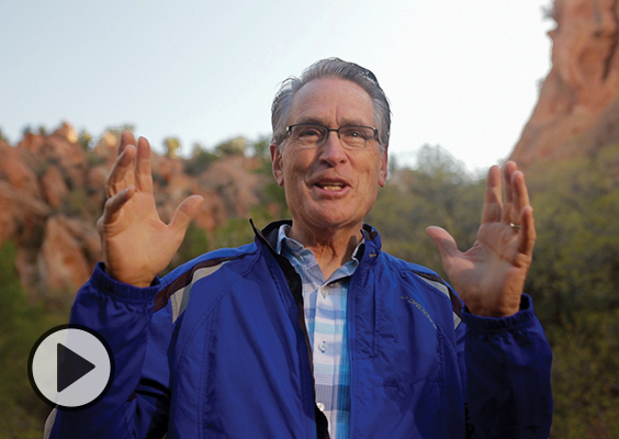Standing in a canyon, BYU professor Arden Pope raises both hands to share his appreciation for clean air.