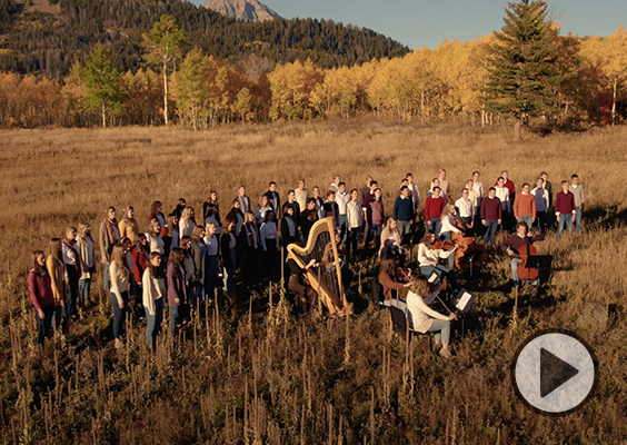 The BYU Concert Choir sings in an alpine meadow surrounded by trees in fall colors.