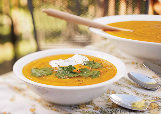 Orange pumpkin soup topped with herbs and cream is served in a white bowl.