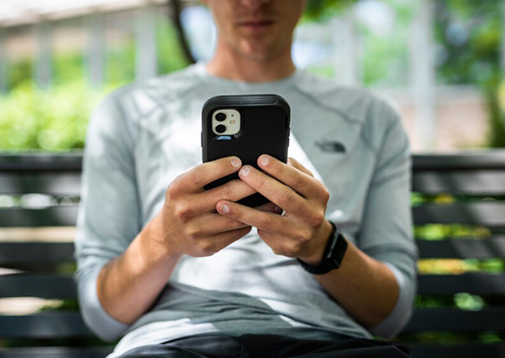 A young man sits on a park bench, intently viewing the screen of a smartphone. Photo by Nate Edwards, BYU Photo.