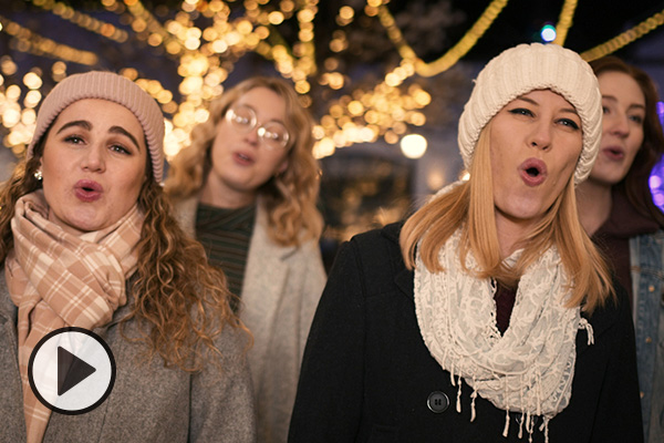 BYU Singers perform White Christmas outdoors amid trees decorated with strings of lights.
