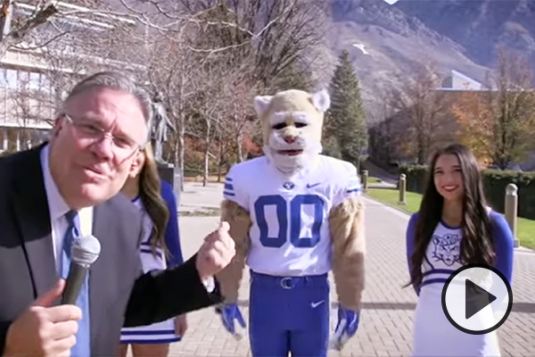 Brad Wilcox with a microphone on campus, interviewing Cosmo and cheerleaders.