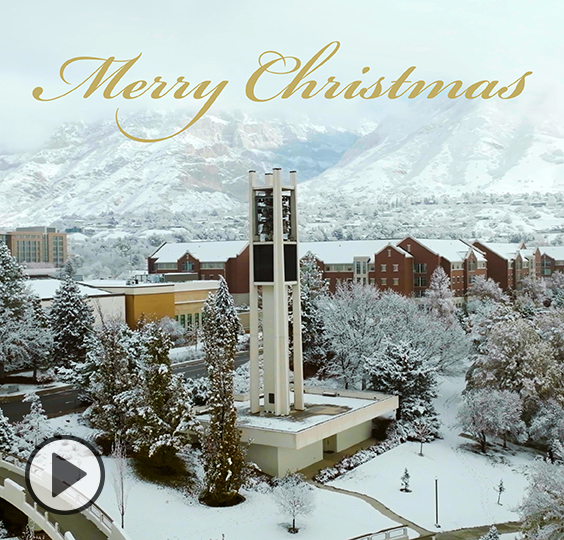 Merry Christmas in gold text floats above the bell tower on a snow-covered BYU campus. The bell tower mtas  Photo by Bradley Slade.