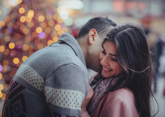 A couple embraces in front of holiday lights to illustrate a new study from BYU identifying three common reasons people love Hallmark Christmas movies.