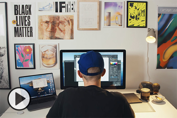 Hunter Young, a student in BYU’s graphic design program, sits at a computer, various posters and art inspiration decorate the wall.