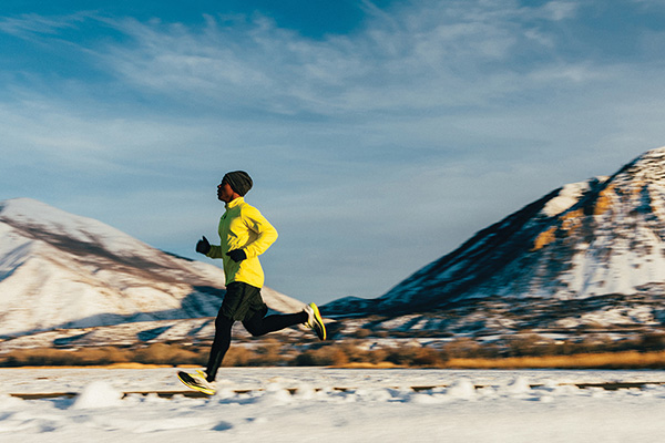 A middle aged male athlete goes for a cold, winter run in Utah, USA during a break in the snow storms. The sky is blue and the sun is shining. He is running to maintain his good mental and physical health and enjoying nature in the winter.