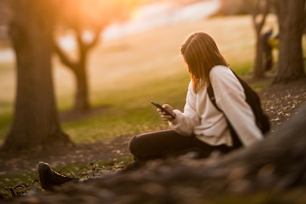 BYU professor Sarah Coyne says moderation is best for young girls' social media use. This photo, by Madeline Mortensen, shows a young women sitting in a wooded area bathed in muted sunlight.