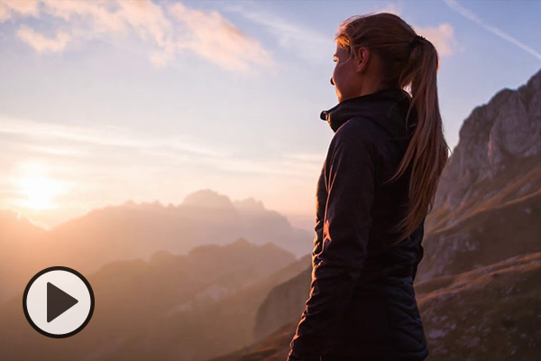 A young woman in an athletic jacket looks at mountains on the horizon.