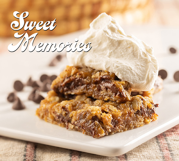 The words Sweet Memories accompany a closeup of moist, gooey, carmelitas with melted chocolate chips and topped with a dollop of whipped cream.