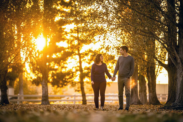 A couple holds hands in a golden-lit rural scene.