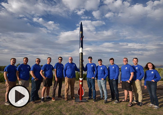 The BYU Rocketry Team poses in the desert with their black and red rocket.