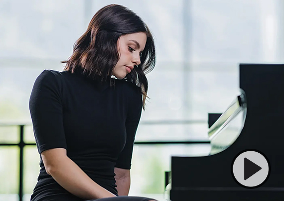 Dressed in concert black, Savannah Jones looks down at a shiny black piano in BYU's Music Building.