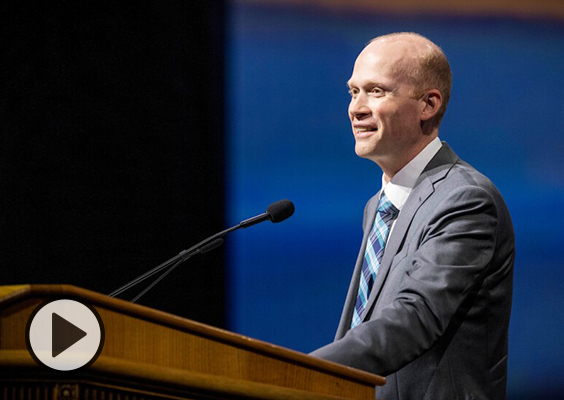 Justin Dyer, professor of Church history and doctrine delivers his devotional address at the podium in BYU's Marriott Center. Photo by Joey Garrison/BYU.