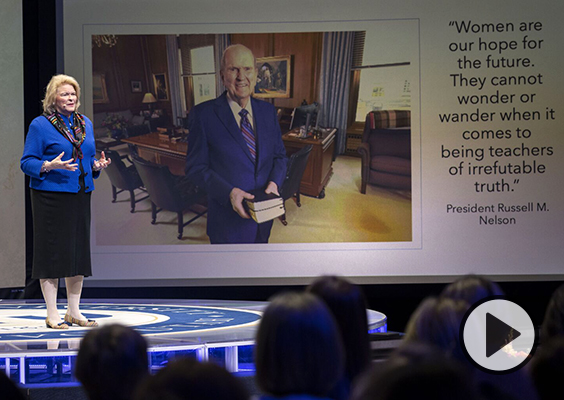 Sheri Dew stands on the stage of BYU's Marriott Center. A slide of President Russell M. Nelson is displayed with the words: Women are our hope for the future. They cannot wonder or wander when it comes to being teachers of irrefutable truth.