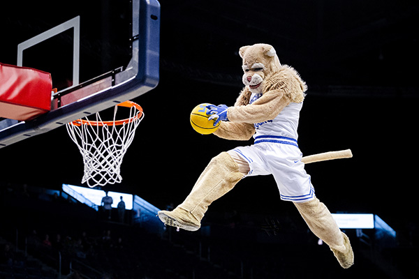 BYU mascot Cosmo the Cougar soars above a basketball rim just before dunking.