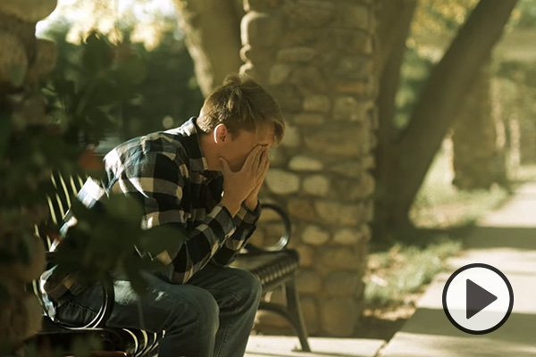 A young man is sitting on a park bench, head in hands.