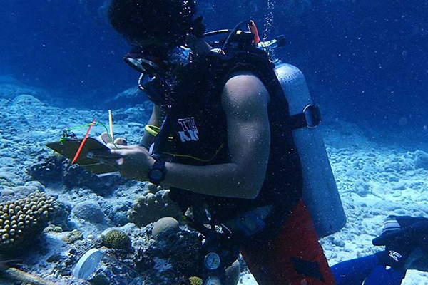 Samoan scientist Stau Segi is underwater wearing scuba gear and taking notes near a coral reef.