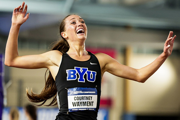 Wearing a black and blue BYU uniform, Courtney Wayment crosses the finish line and wins another championship.