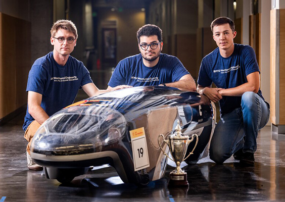Three BYU engineering students crouch around their award-winning supermileage car