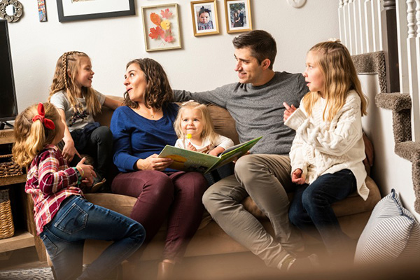 A family gathers on a couch to read a picture book and spend time together.