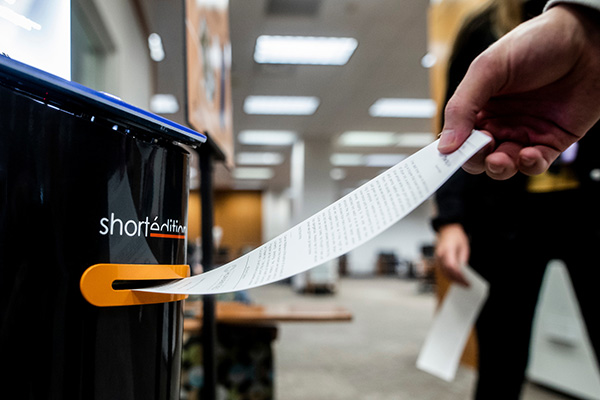 A story on receipt paper is pulled from a dispenser in the BYU library.