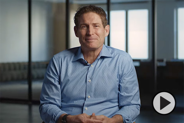 A smiling Steve Young, in a light blue shirt, sits with his hands folded.