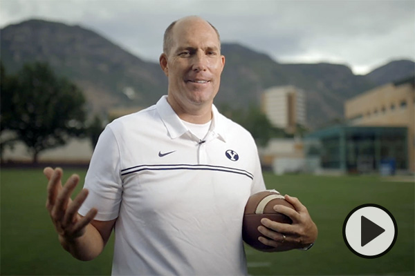 Former BYU and NFL great Chad Lewis holds a football while standing on the practice field at BYU.
