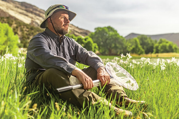 Jim Spencer sitting in a sunlit, grassy mountain meadow, butterfly net in hand.