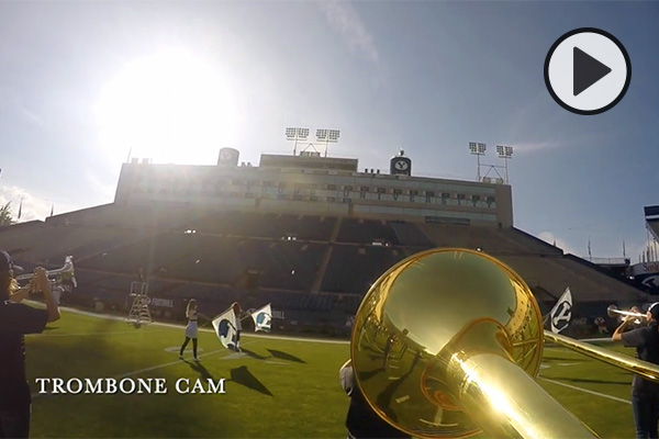 This photo, taken from a trombone cam shows the turf, color guard with Y flags, and the empty seats and press box of at LaVell Edwards Stadium.