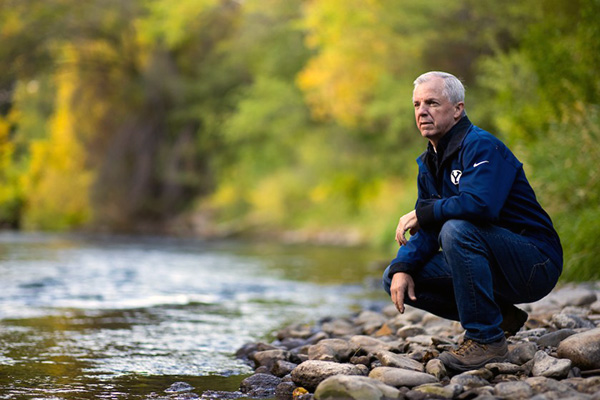 Jim Nelson, dressed all in blue, crouches on rocks near a gently flowing river.