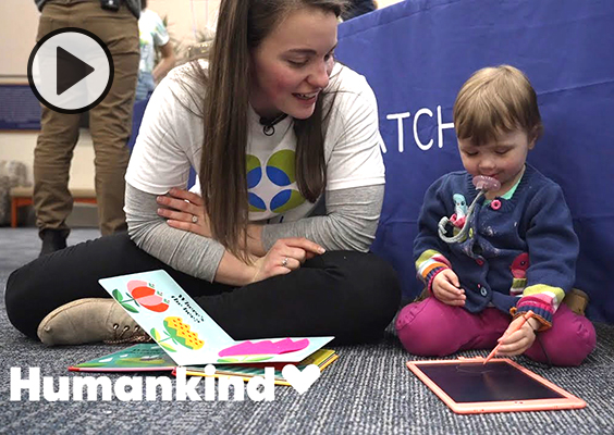 BYU grad Shawen Christenson-Bueckers sits on the floor reading a book with 2-year-old Amelia Bellemore.