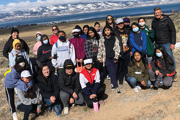 A Salt Lake City–based Scout troop for refugee girls pose for a photo above mountains and a lake.