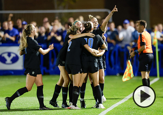 BYU women's soccer players gather in a celebration huddle. One player points her index finger to the sky.