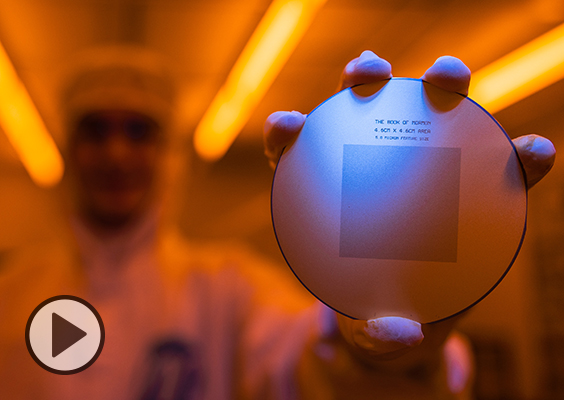 An engineer in clean room gear holds up a circular silicon wafer etcehd with the entire text of the Book of Mormon.